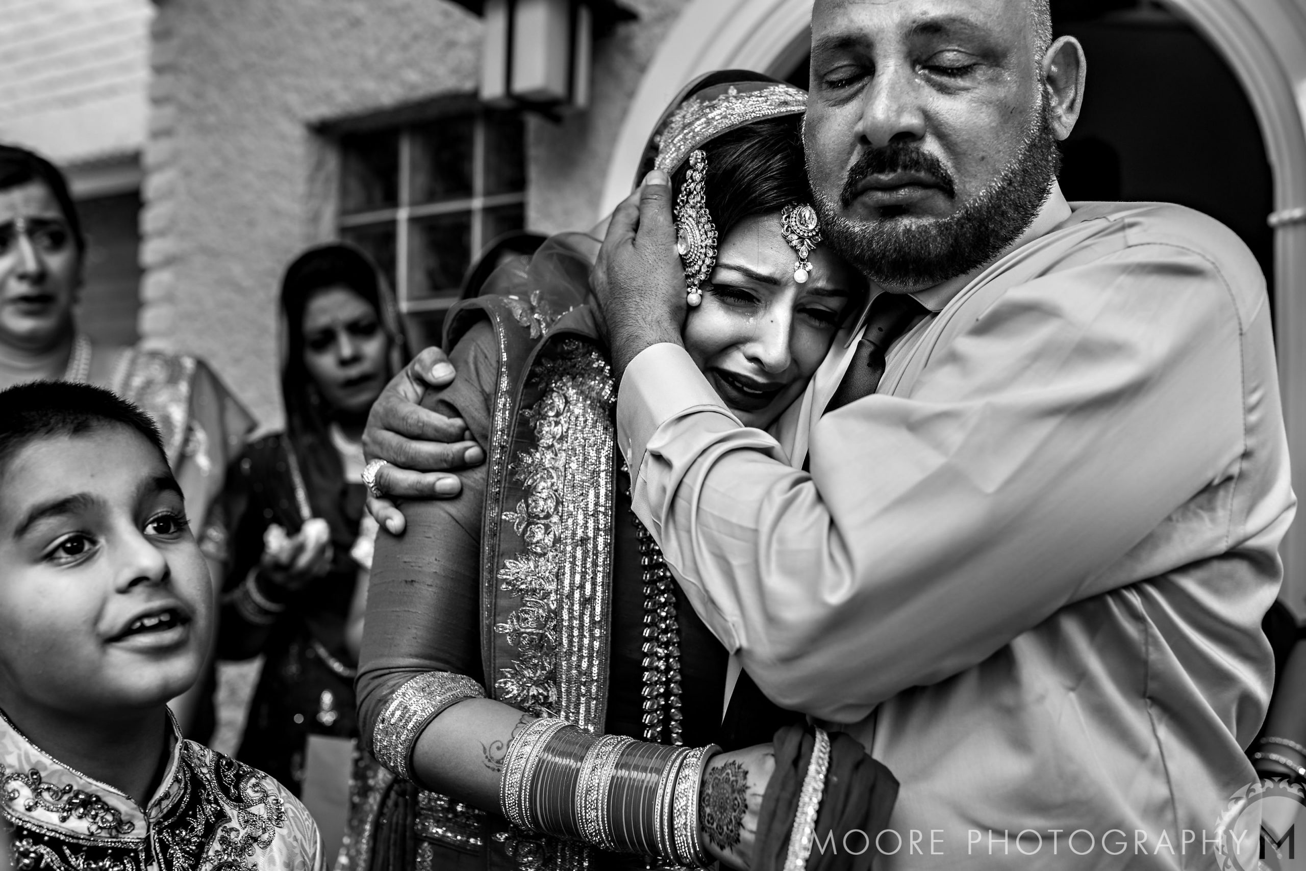Bride crying, embracing a man in an Indian wedding, surrounded by family in emotional farewell.