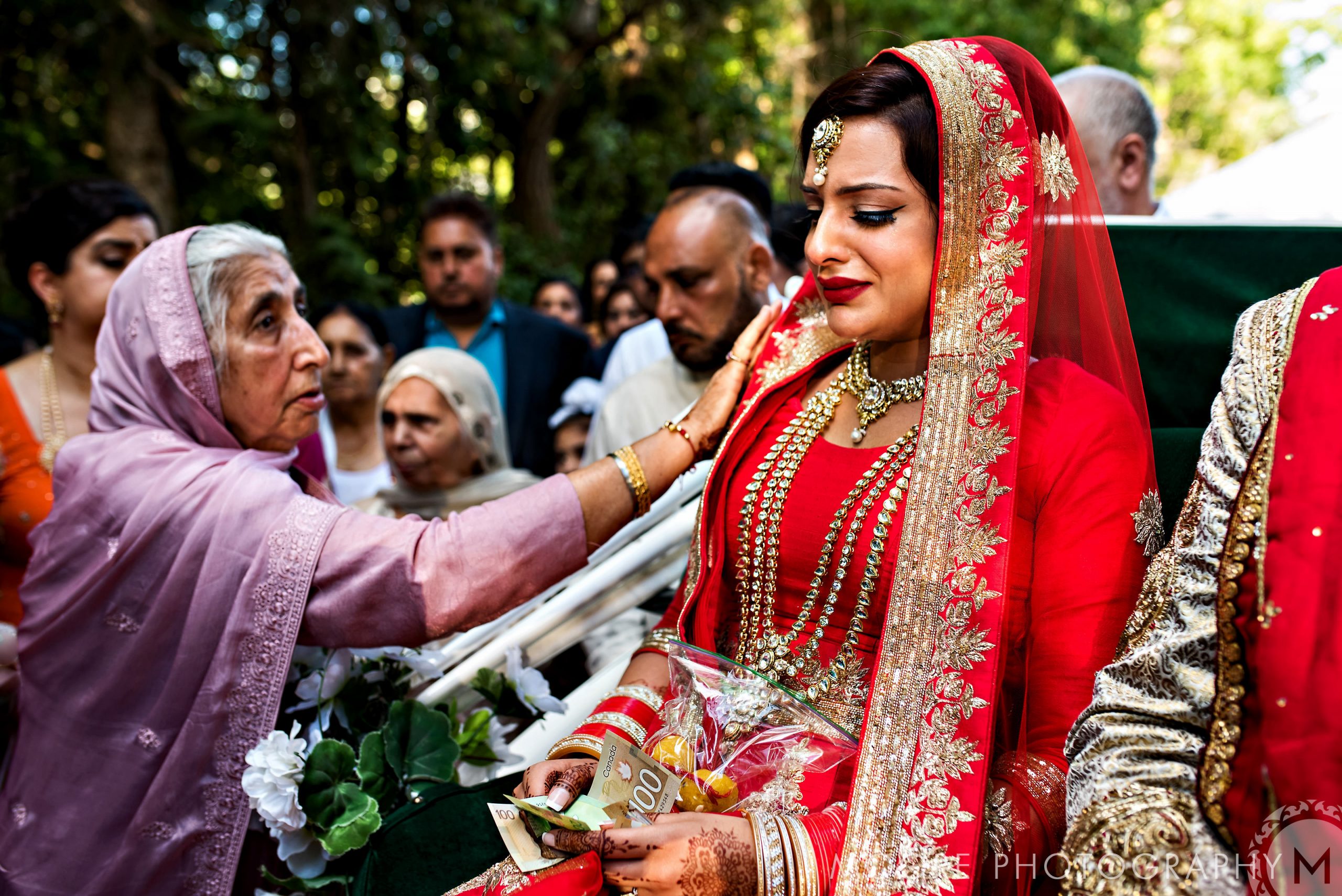 During an Indian wedding, the bride in red receives blessings from an elder woman.
