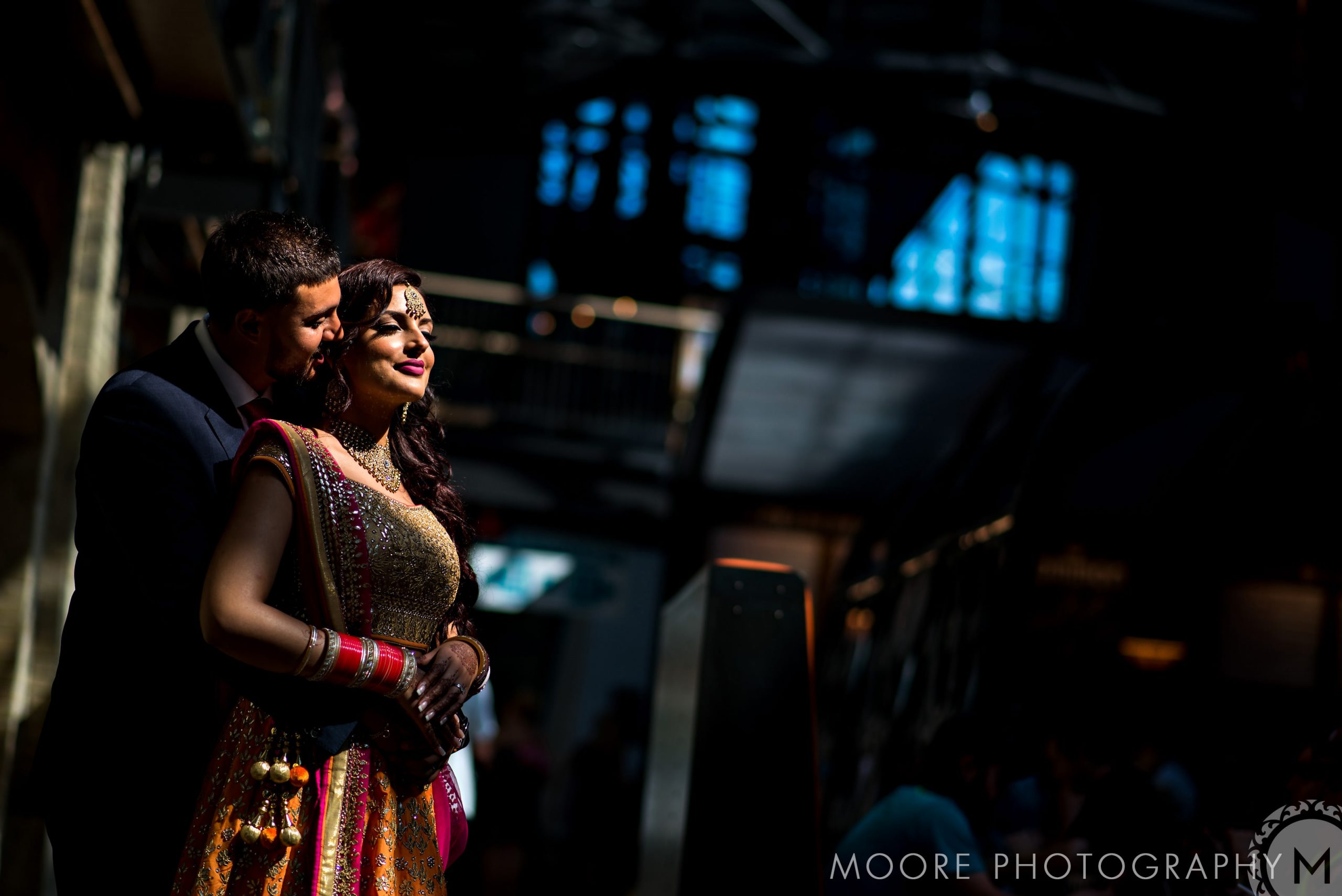 Couple in Indian wedding attire sharing an intimate moment in a softly lit room.