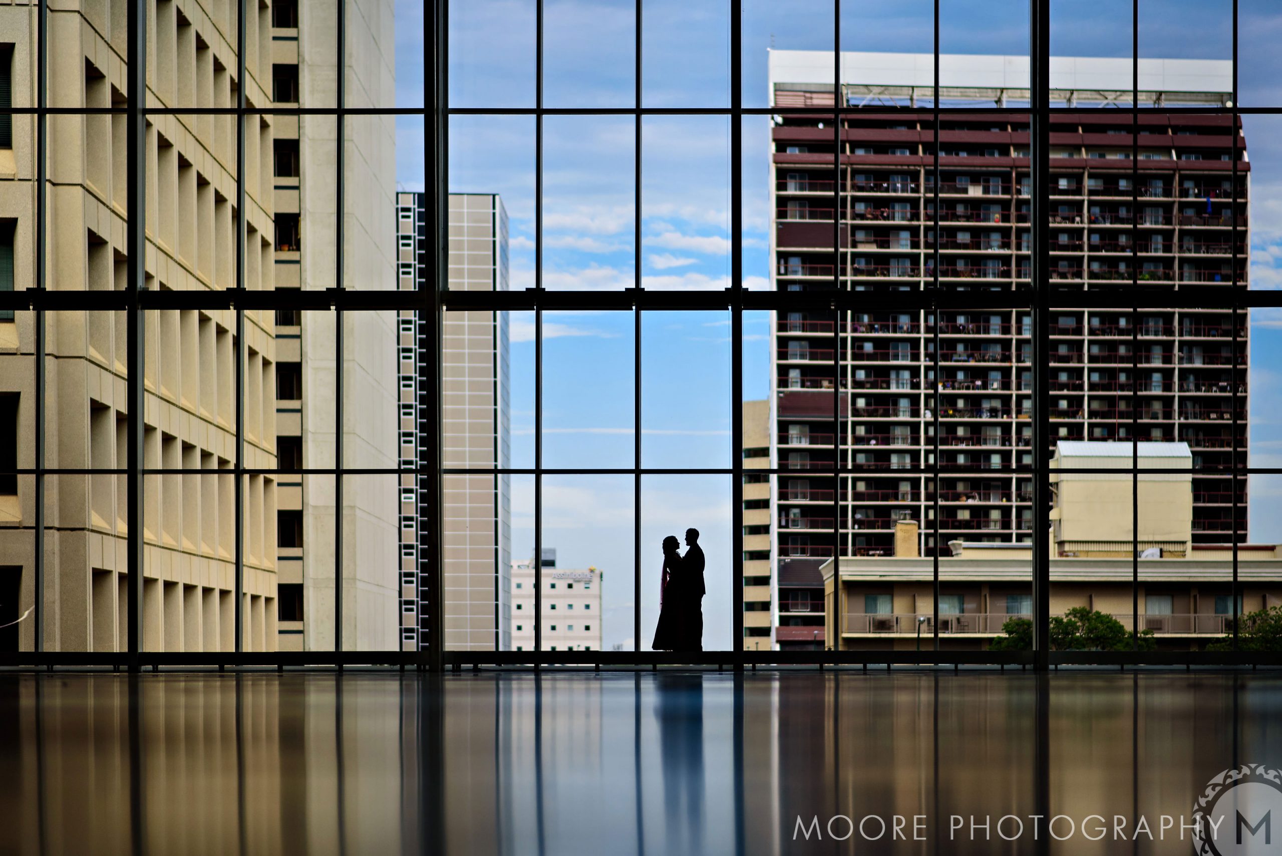 Silhouetted couple stands in glass atrium overlooking Winnipeg's city buildings.