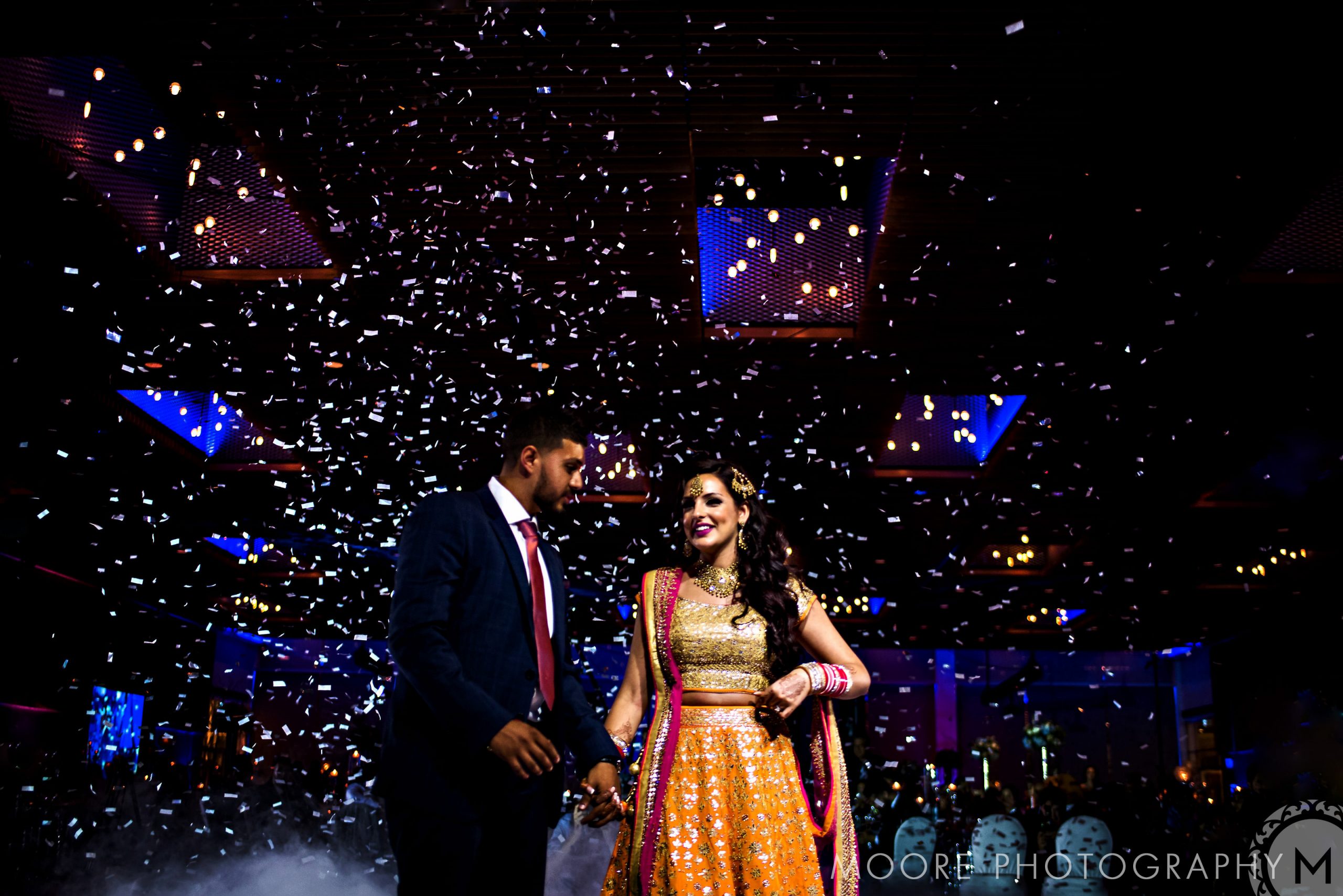 A couple dances under confetti at a festive, colorful Indian wedding celebration.