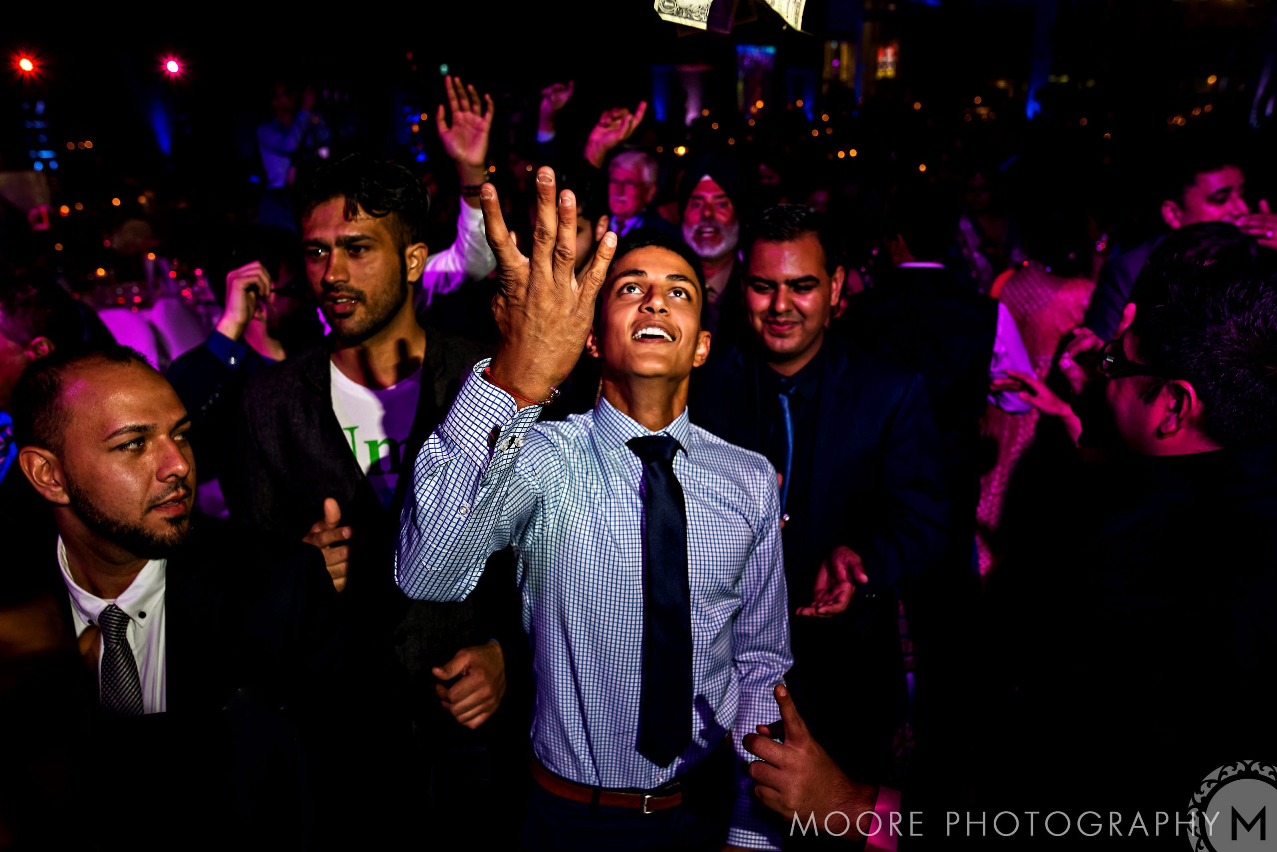 At a lively Indian wedding, a man in a shirt and tie throws money in the air.
