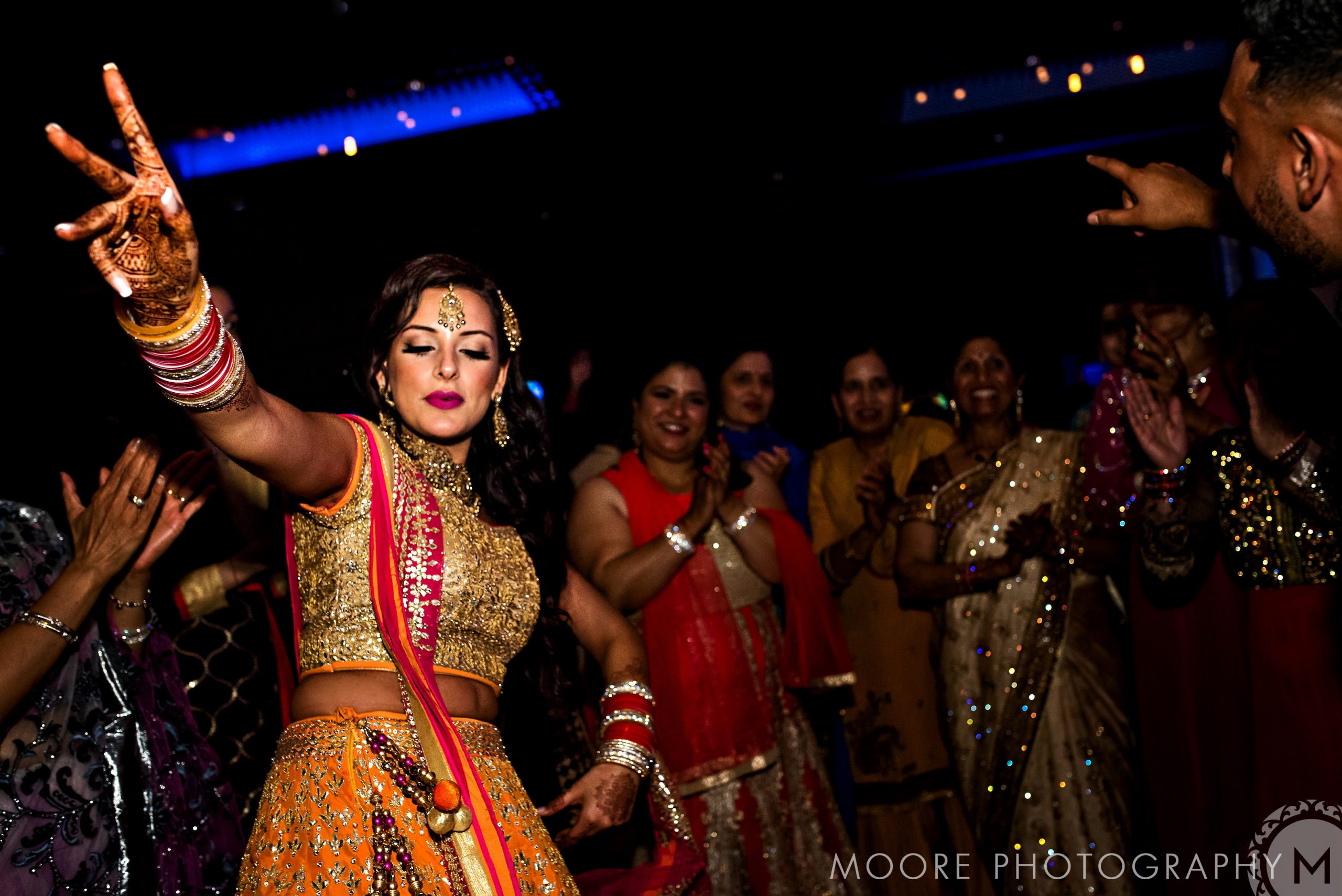 Woman in traditional attire dancing at a lively Indian wedding celebration with onlookers.