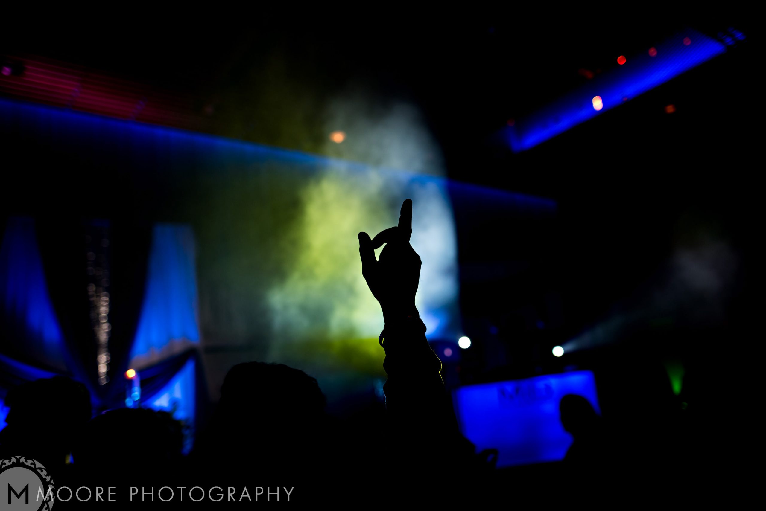 Silhouette of a raised hand at a vibrant, smoke-filled Indian wedding celebration.