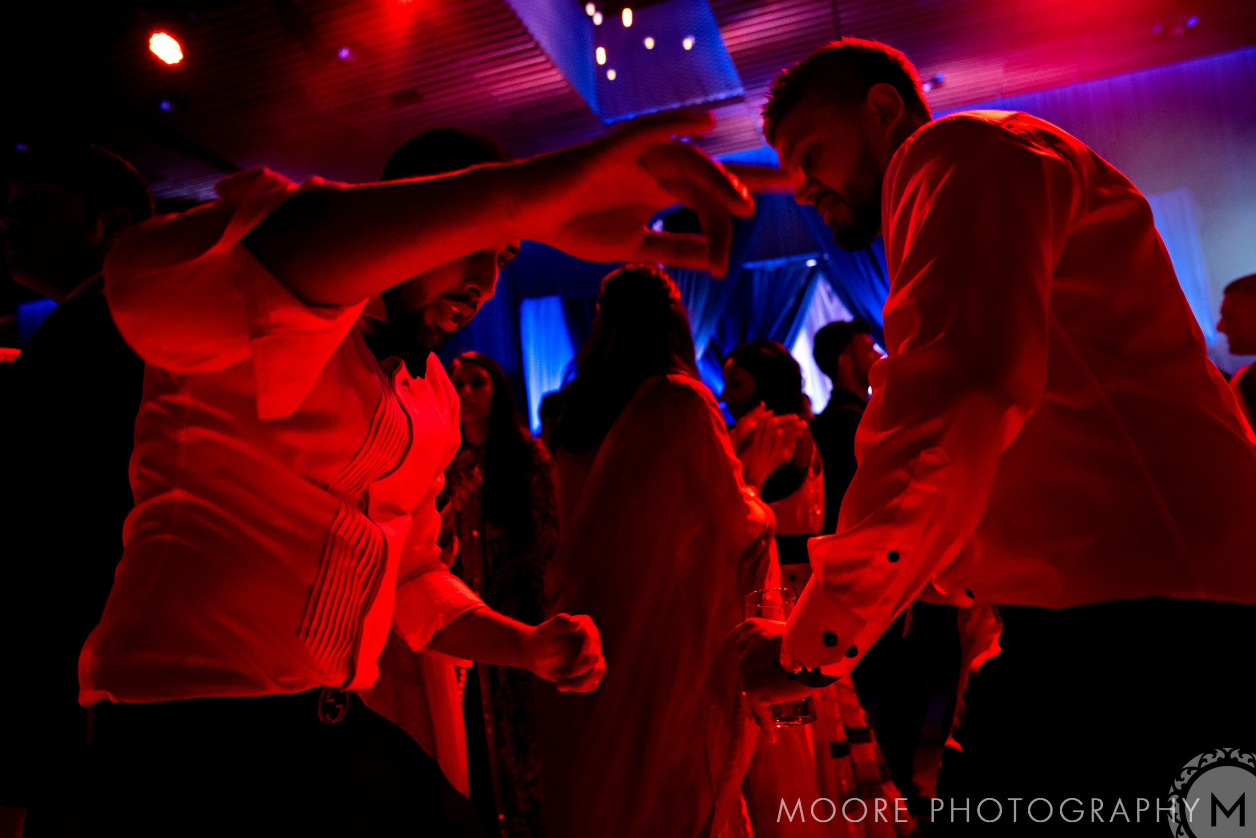 Guests dancing energetically at an Indian wedding with red and blue lights.