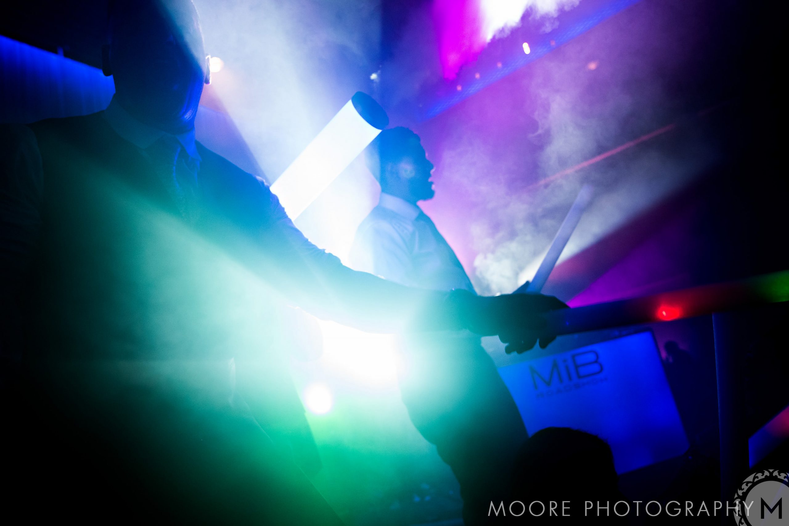 Silhouetted performers glow in colorful lights at an Indian wedding celebration.