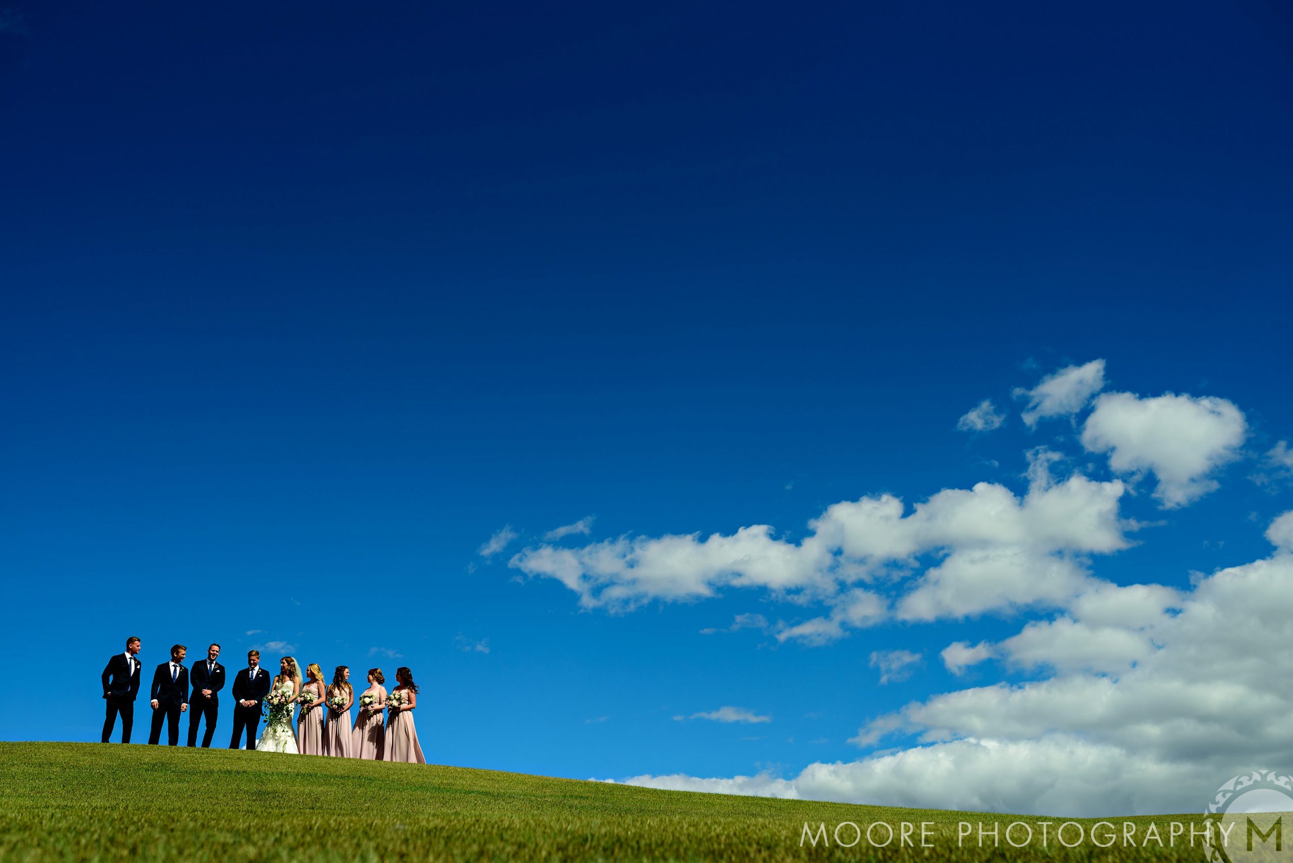 Winnipeg wedding venues host parties on grassy hills under a bright blue, cloud-dotted sky.