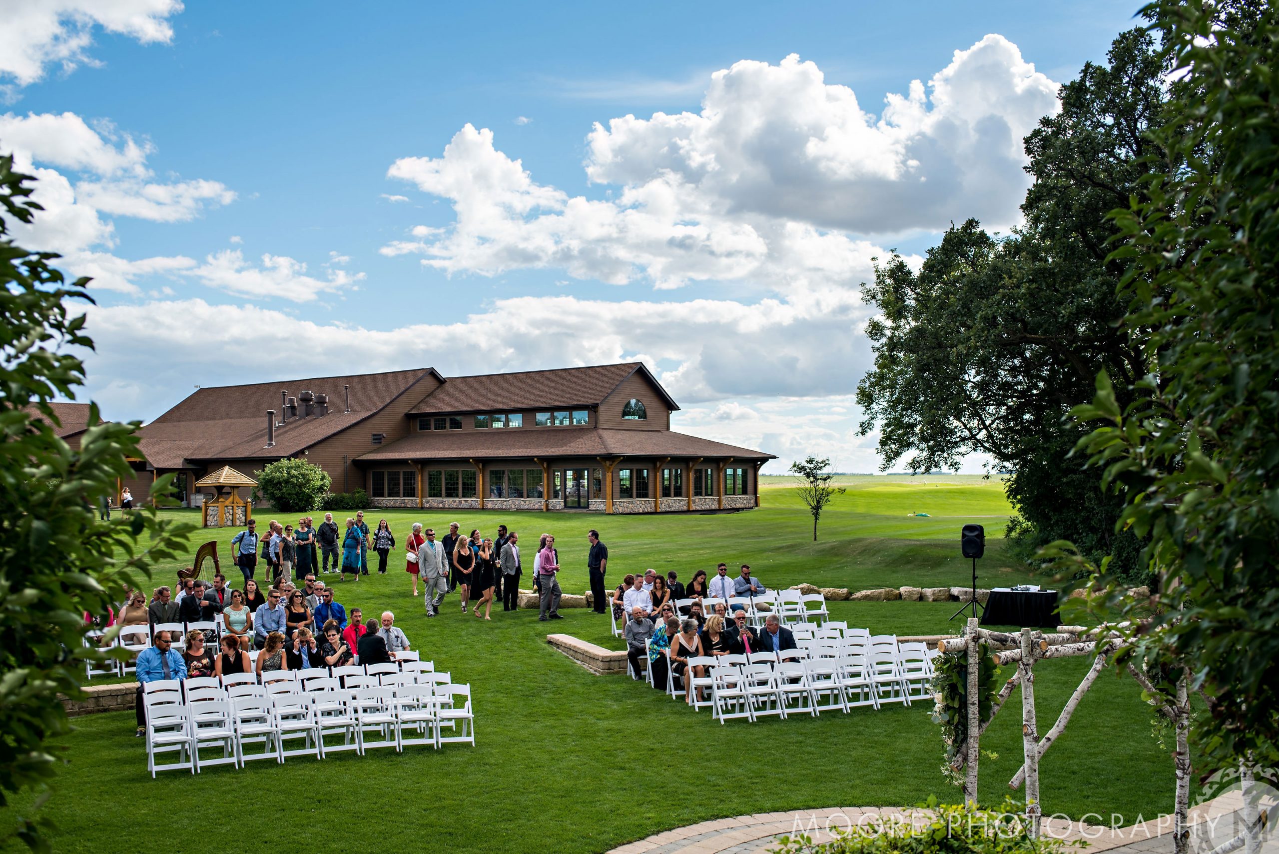 Outdoor ceremony at Winnipeg wedding venues, guests on white chairs, large building behind.