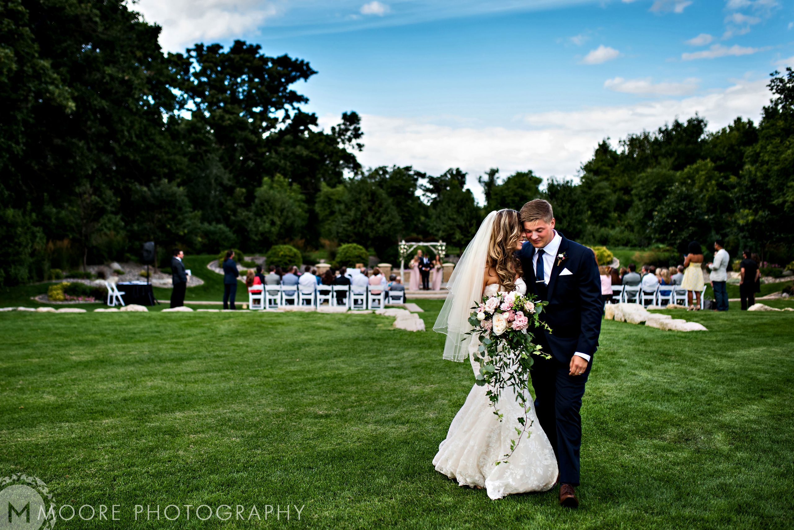 Bride and groom stroll on grass at a charming Winnipeg wedding venue.