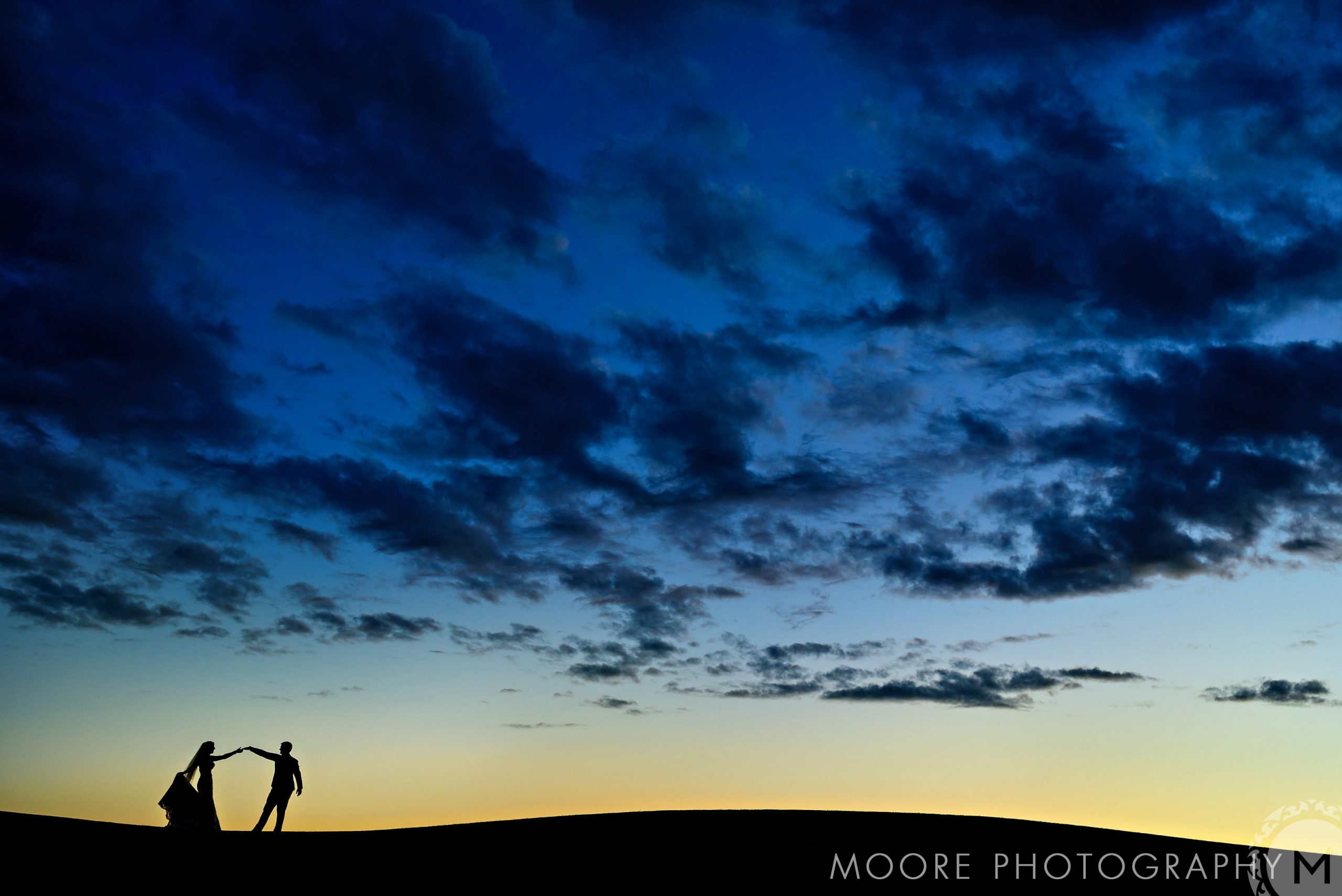 Silhouetted couple dances against a dramatic Winnipeg sunset sky with scattered clouds.