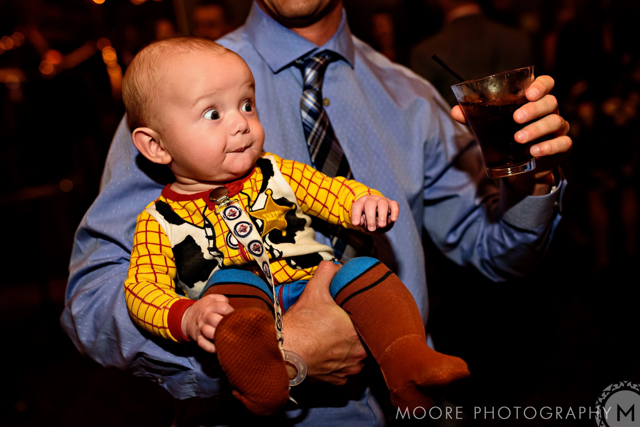 Baby in Woody costume held by a man celebrating at a Winnipeg wedding venue.