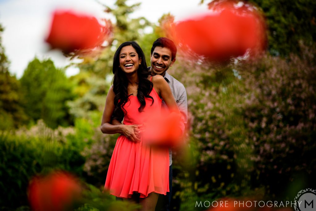 And engaged, embracing and laughing with trees in the background and colourful tulips in the foreground in a assiniboine park in Winnipeg