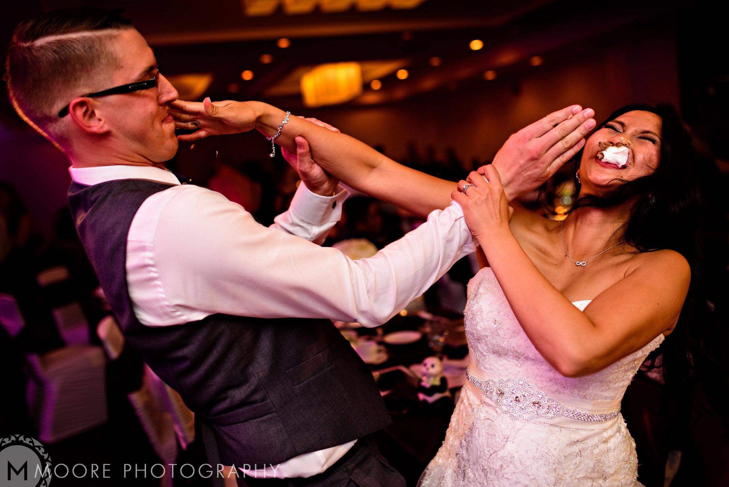Couple playfully smearing cake at a Winnipeg wedding reception.
