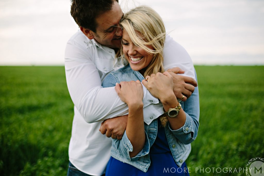Couple embracing and smiling in a green field.