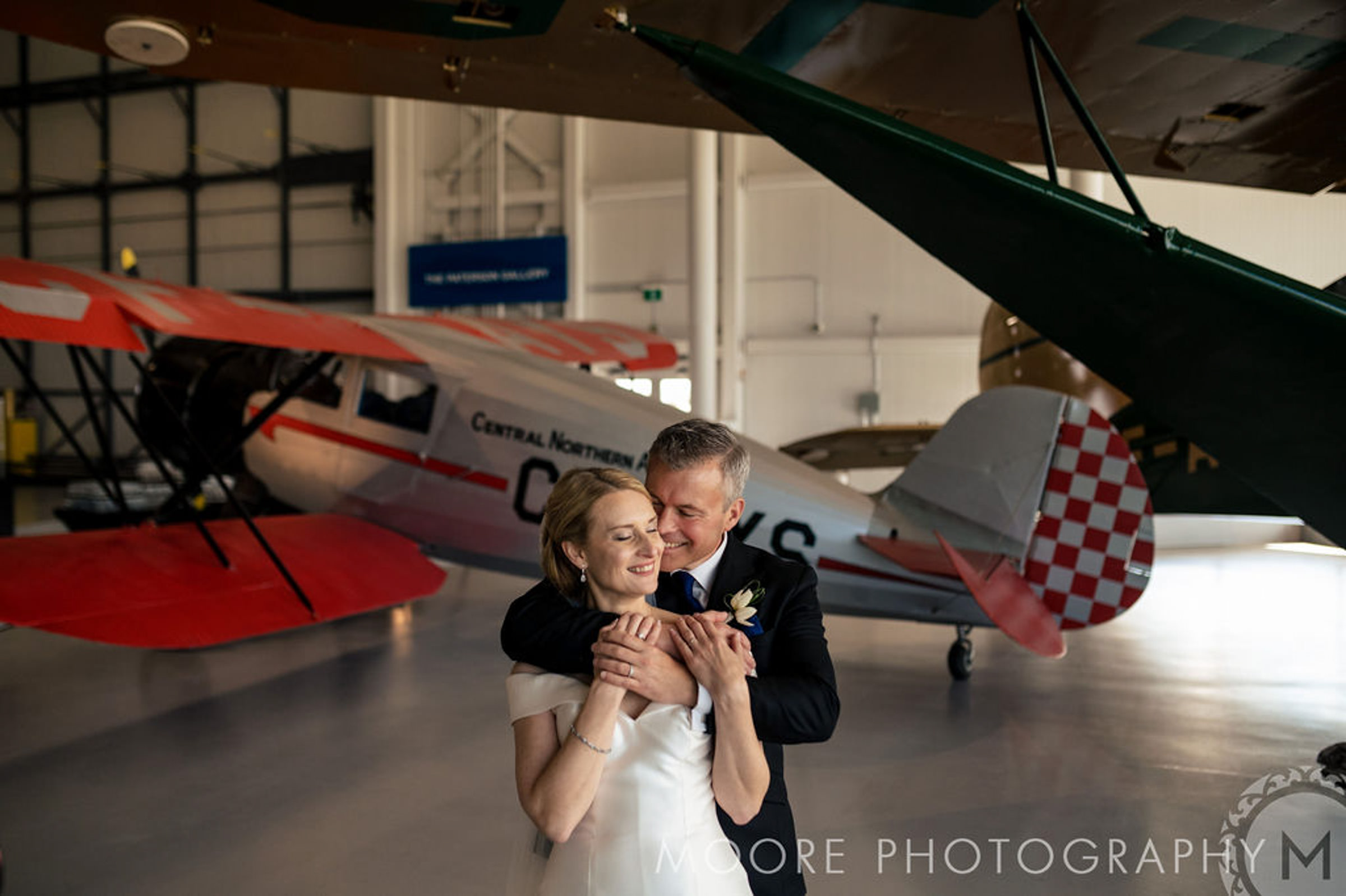 A couple embraces in front of vintage airplanes at a Winnipeg wedding venue.