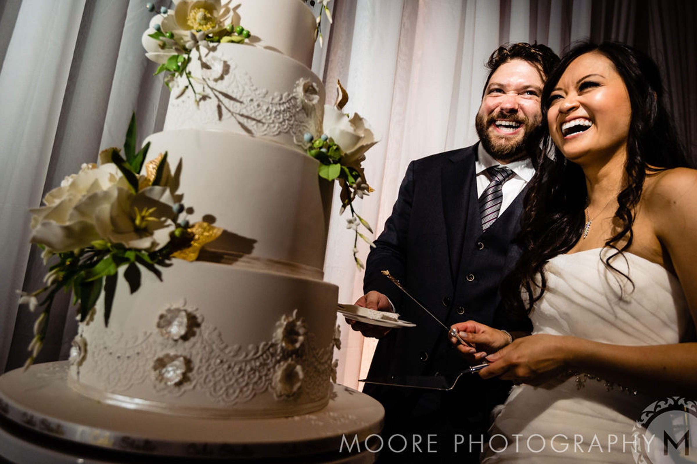 Couple joyfully cutting a tiered white cake at a beautiful Winnipeg wedding venue.