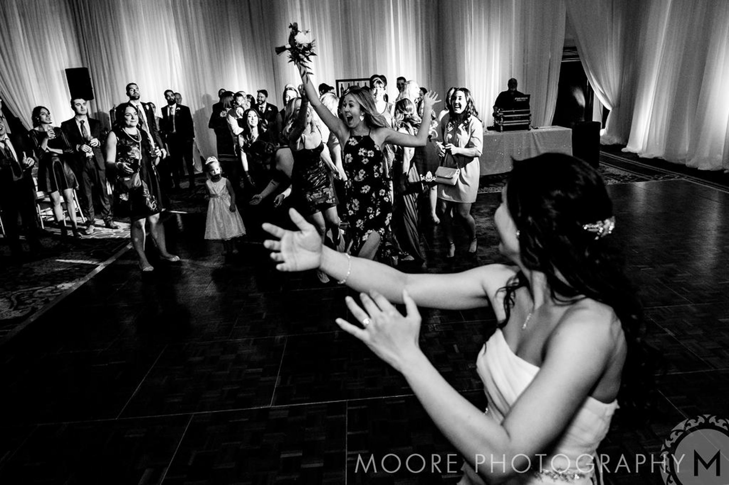 Bride tosses bouquet at excited guests on Winnipeg wedding venue dance floor.