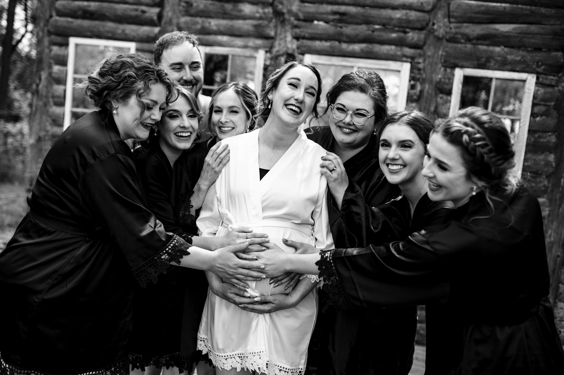 Group of smiling women in robes gathered around pregnant woman outside a Winnipeg wedding cabin.