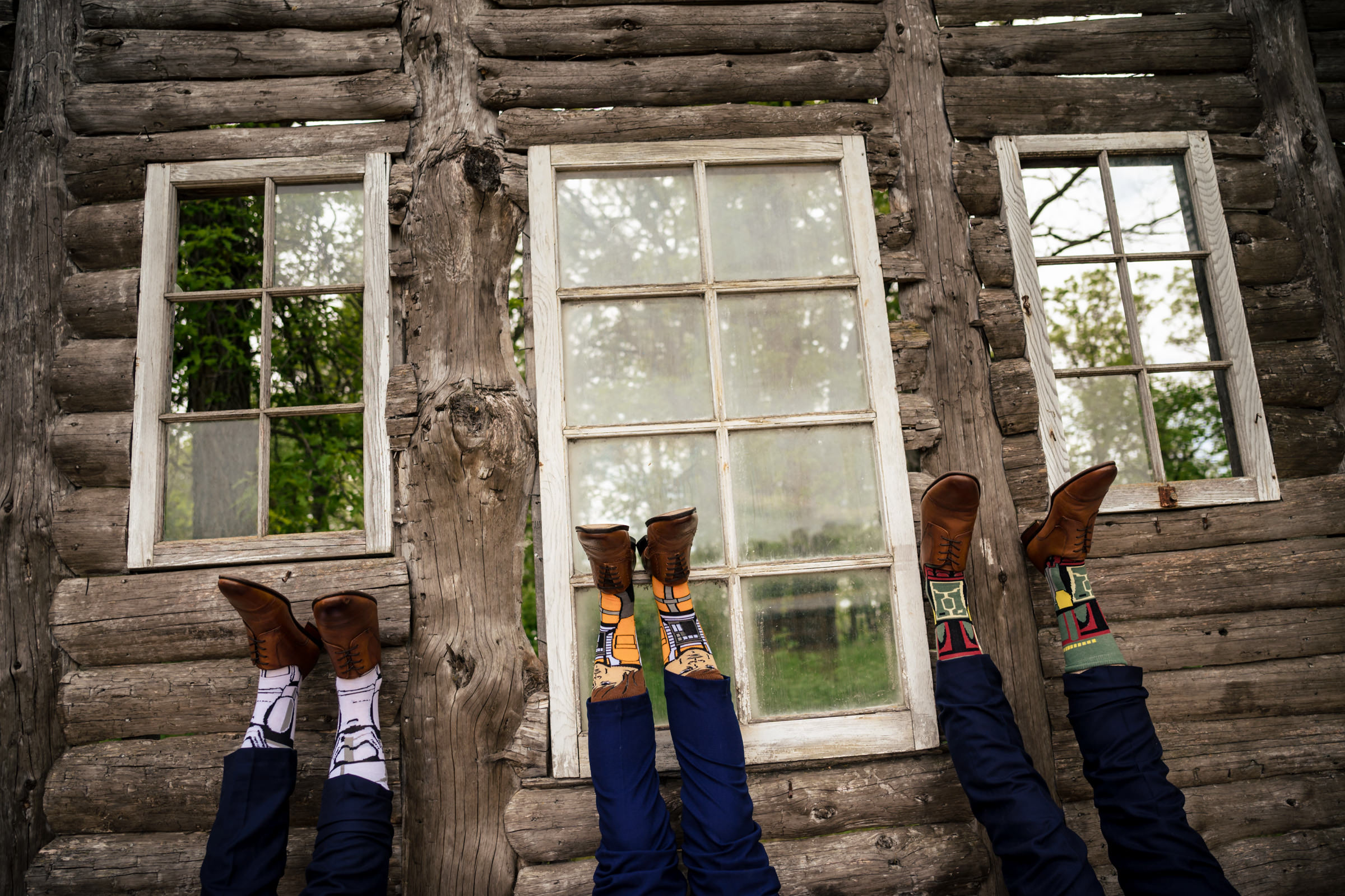 Four people upside down against a log wall, showcasing colorful socks and brown shoes in Winnipeg.