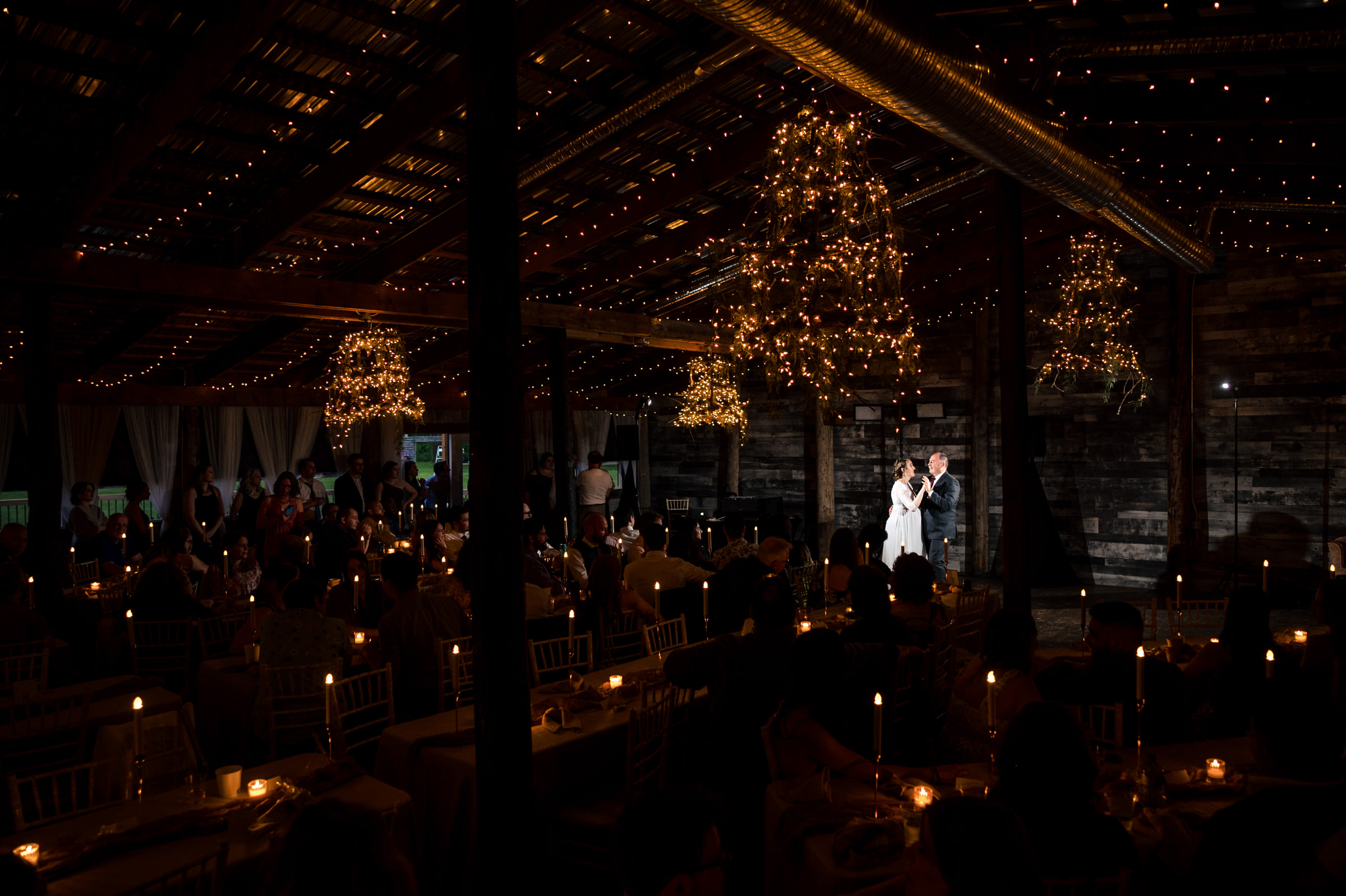 Couple dancing under string lights in a dimly lit Winnipeg wedding venue barn.