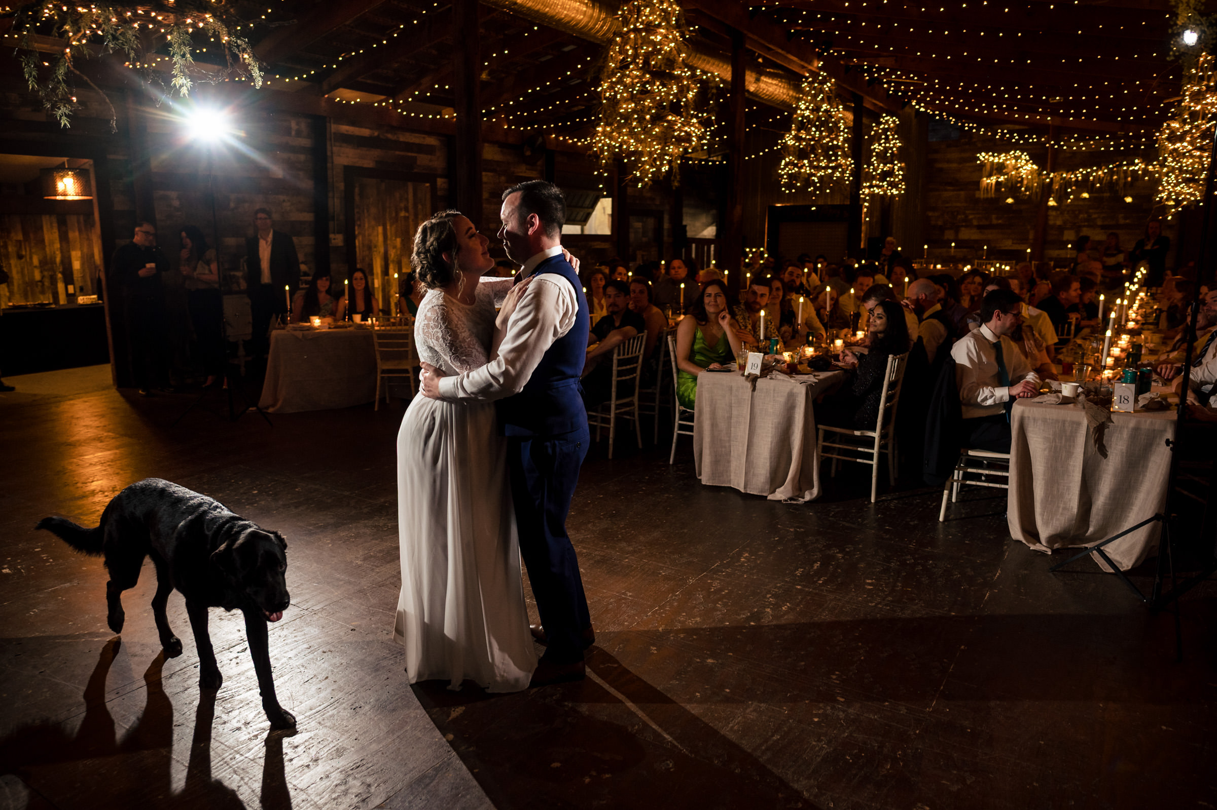 Couple dancing at a Winnipeg wedding venue; guests under string lights with a black dog.
