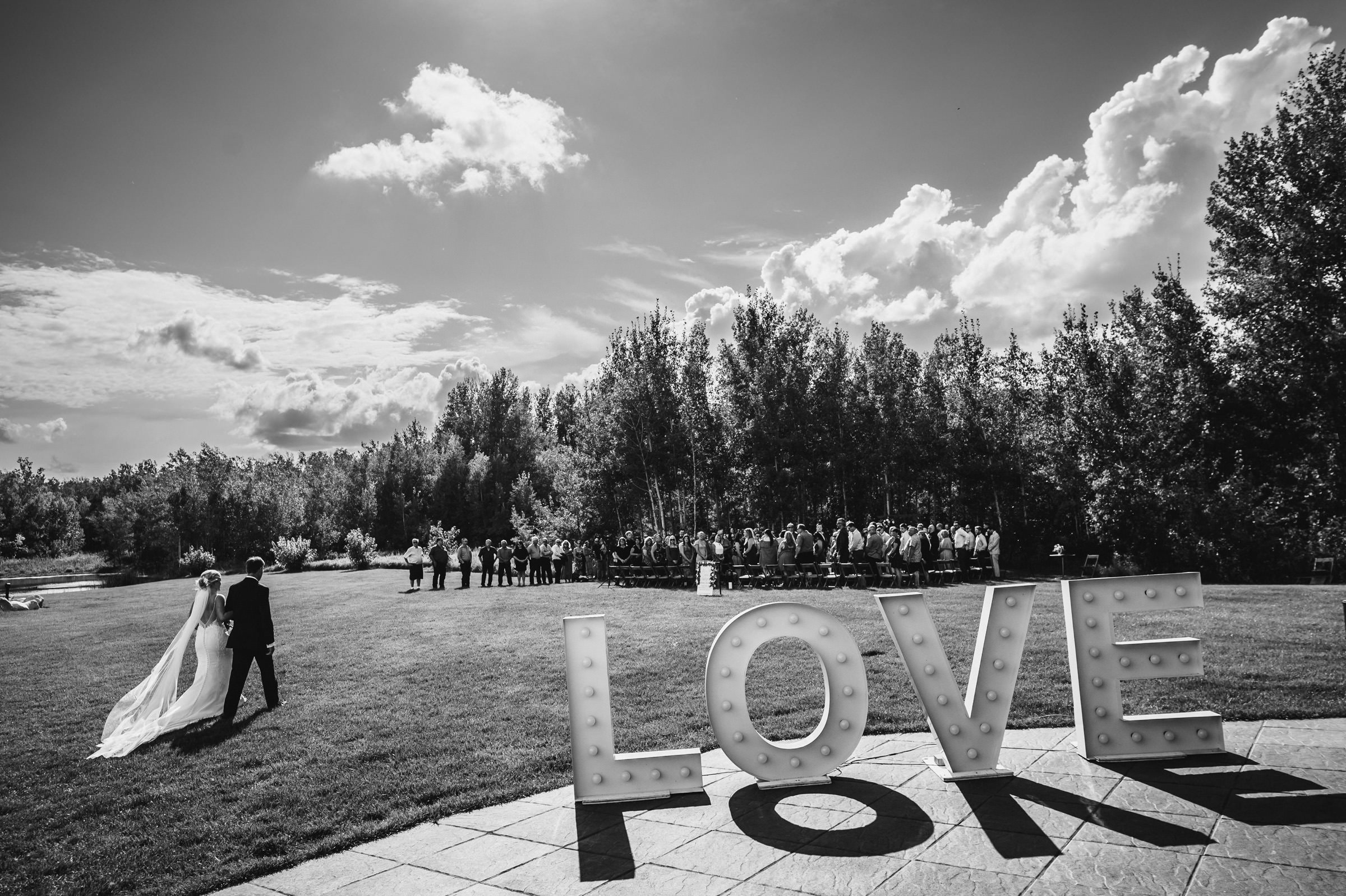 Bride and groom walk toward guests; "LOVE" sign highlights Winnipeg wedding venue.