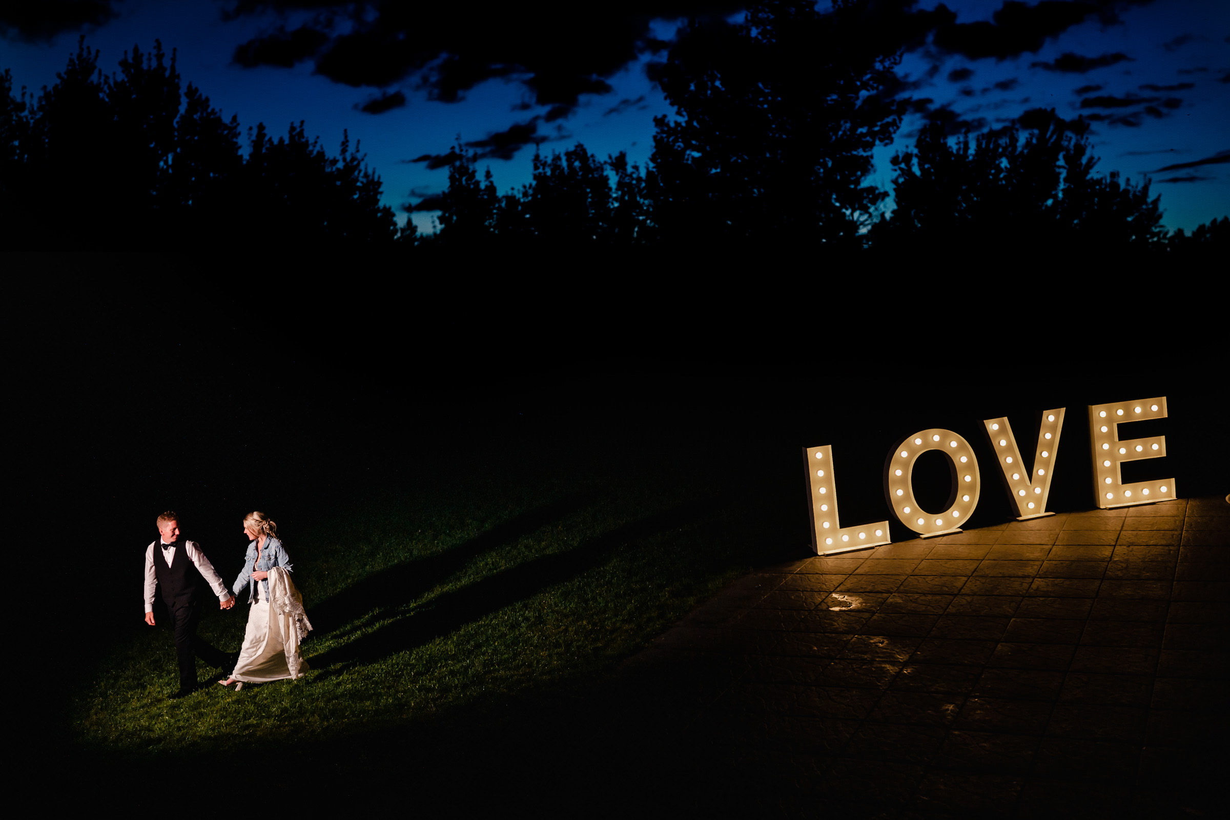 Couple strolls at night near "LOVE" sign, perfect for a Winnipeg wedding venue.