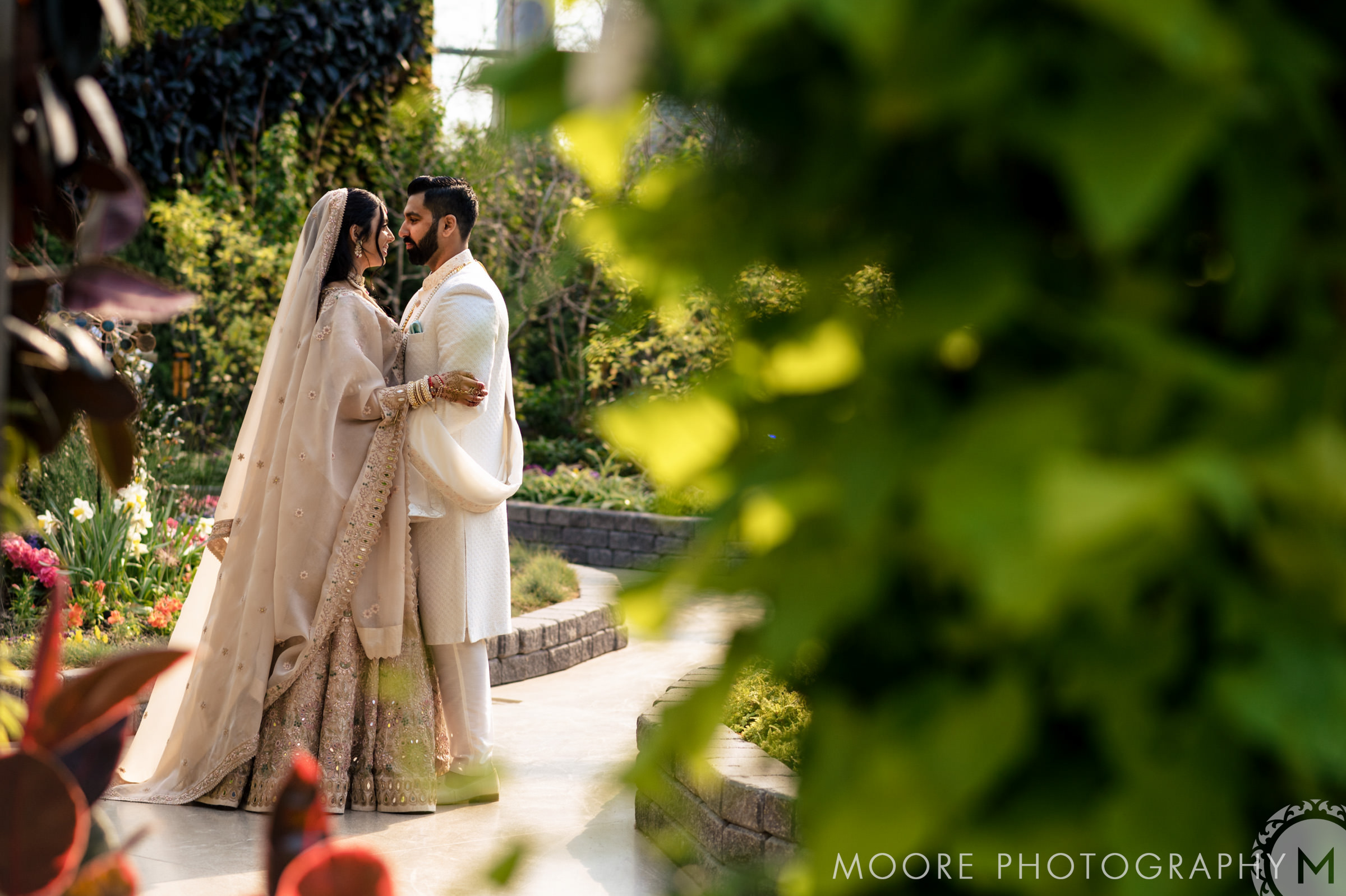 A couple in elegant attire embraces in a lush Winnipeg wedding garden.