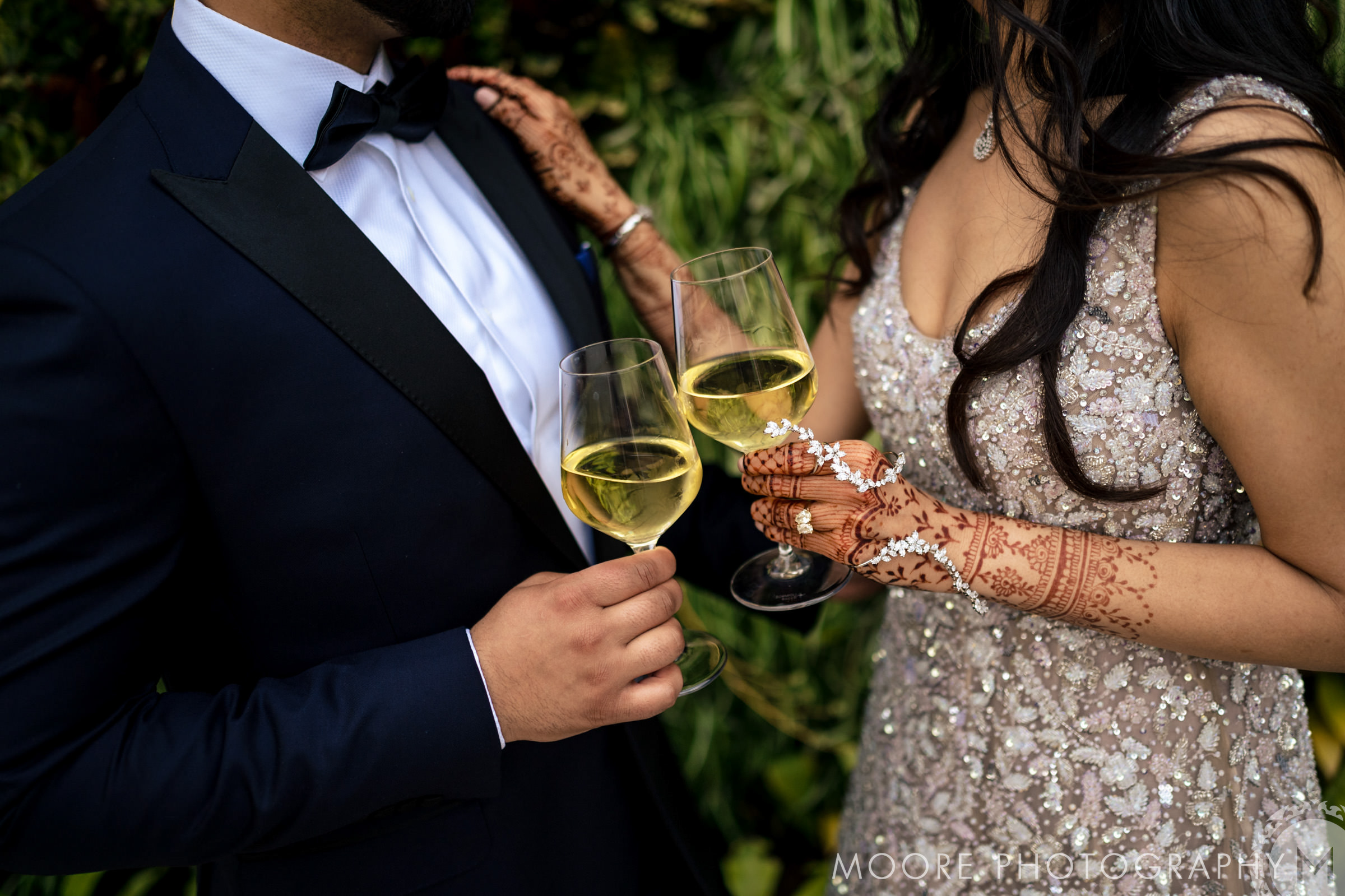 Couple in formal attire at a Winnipeg venue, clinking champagne, henna on woman's hands.