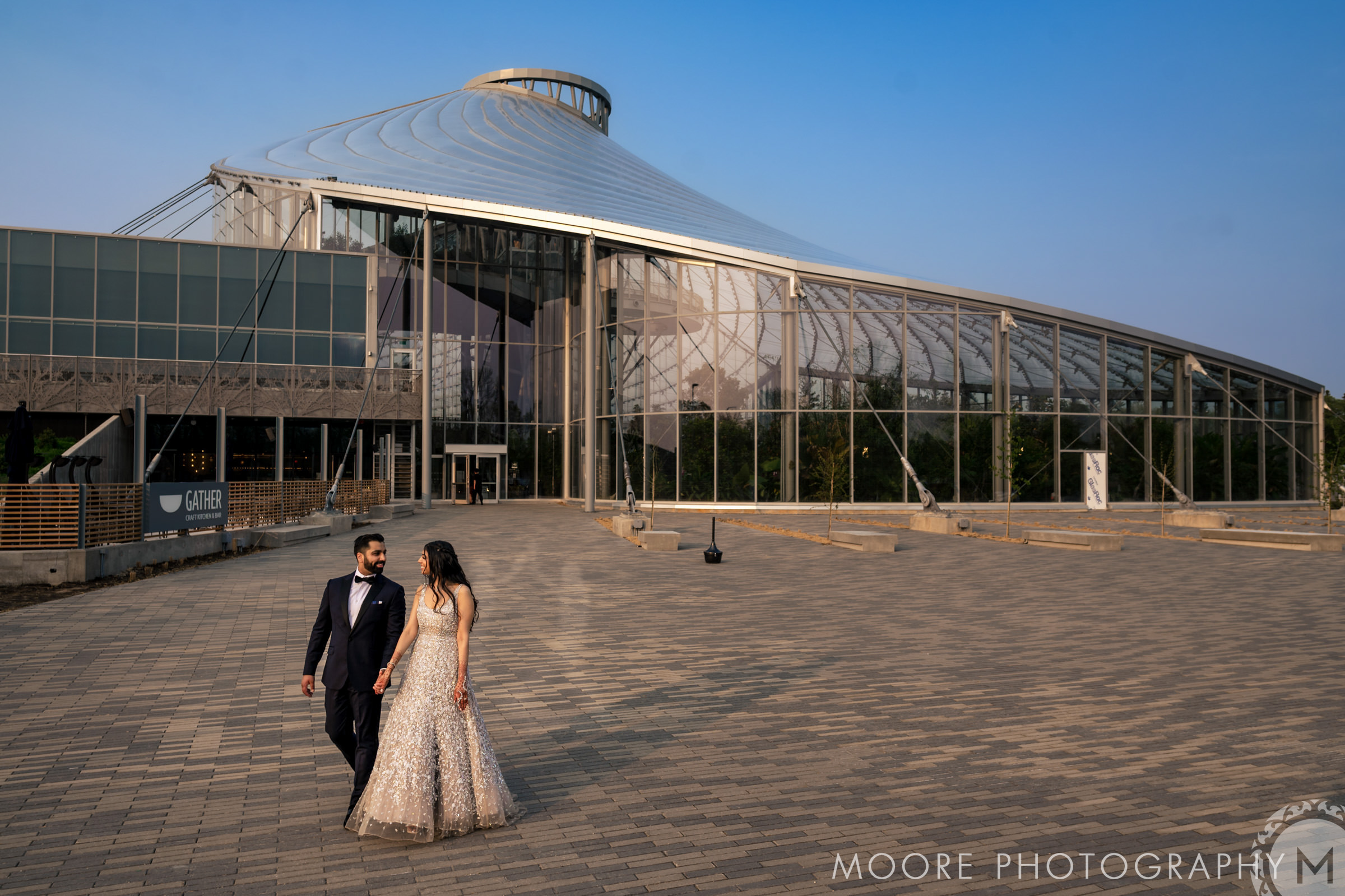A couple strolls elegantly before a modern glass building, perfect for Winnipeg wedding venues.