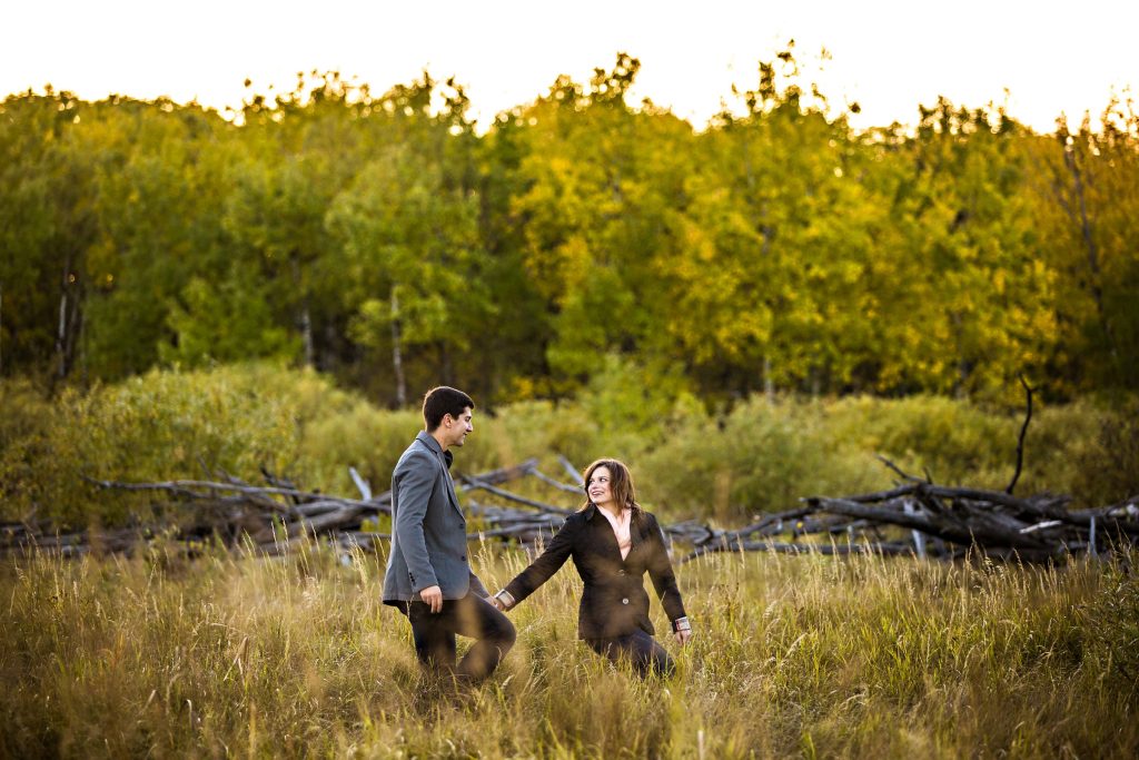 An engaged couple, holding hands and walking down a path at Assiniboine Forest