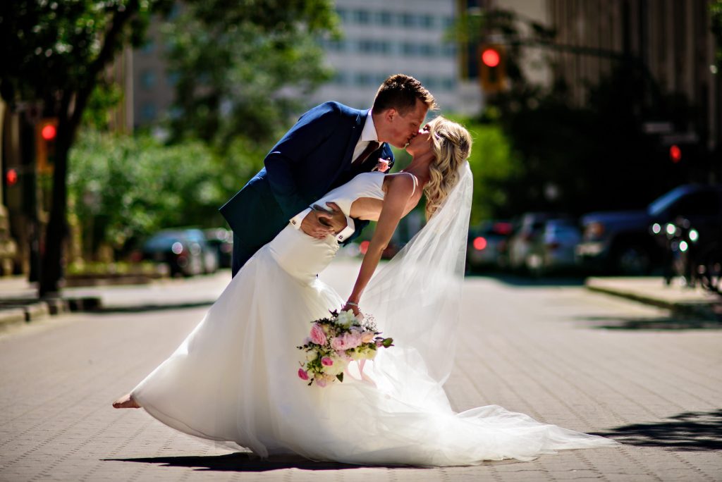 At Groom, dipping his bride, while kissing her in the middle of a city Street in downtown Winnipeg, Manitoba