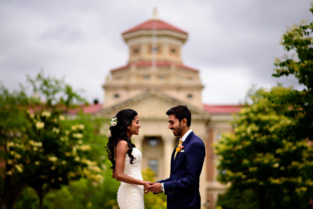 A bride and groom holding hands and laughing in front of a building in Winnipeg Manitoba