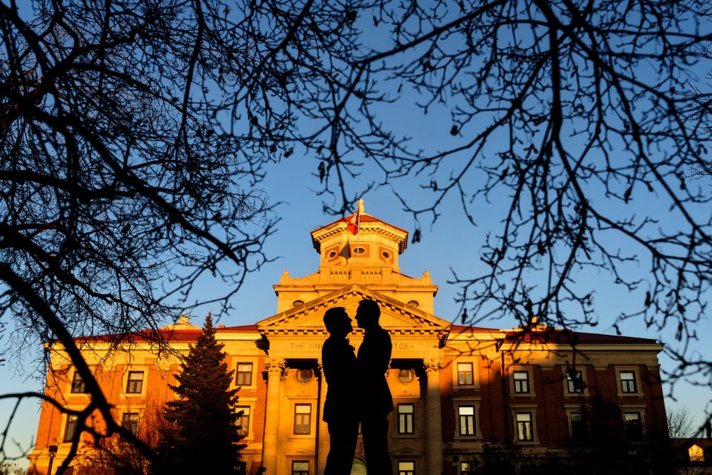 A silhouette of a couple on their wedding day posing in front of an old building with trees