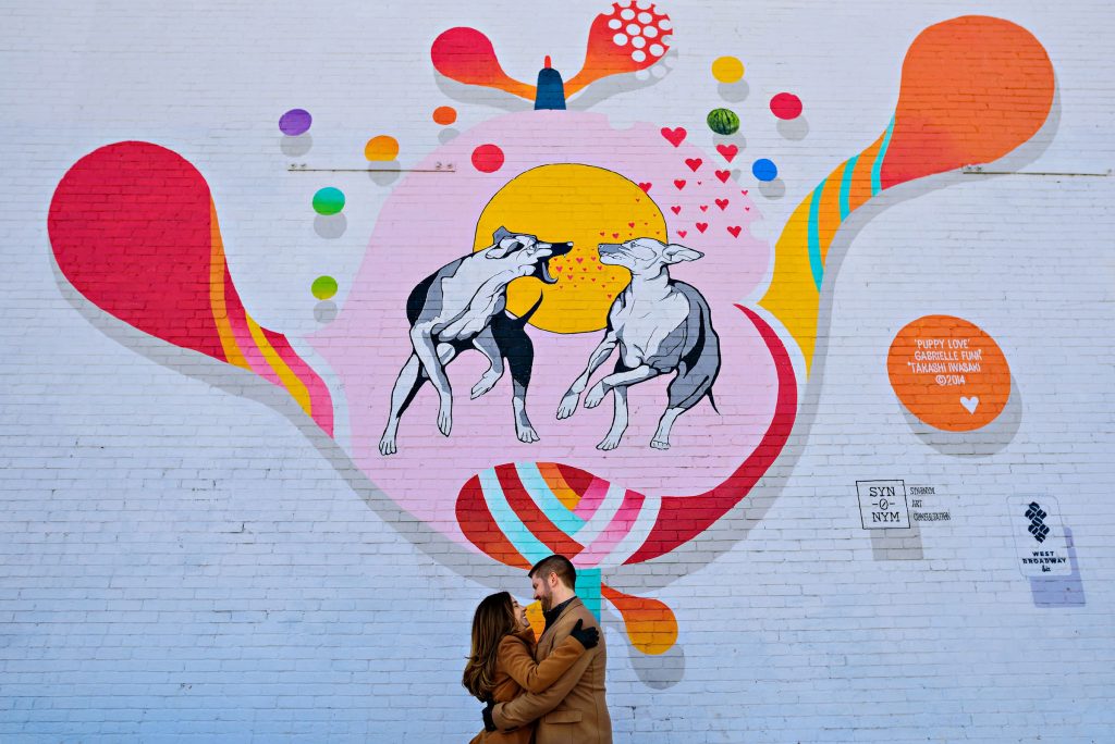 An engaged couple embracing in front of a mural in downtown Winnipeg
