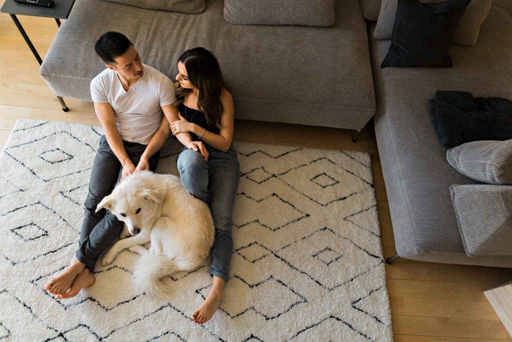 An engaged couple with their dog sitting in their living room for engagement photo