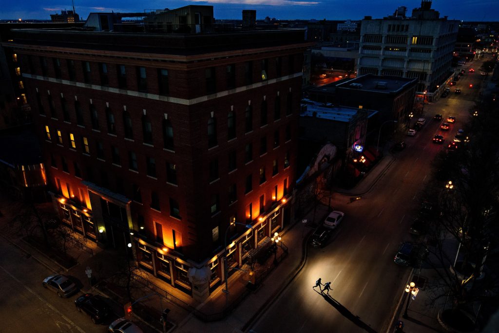 Shadows of a couple, running in a spot of light across the street between buildings in the downtown Winnipeg exchange district