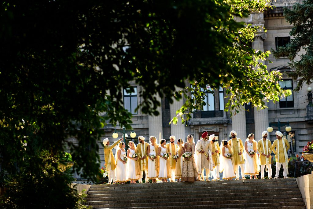 A large wedding party, laughing, and talking together at the Winnipeg legislative building