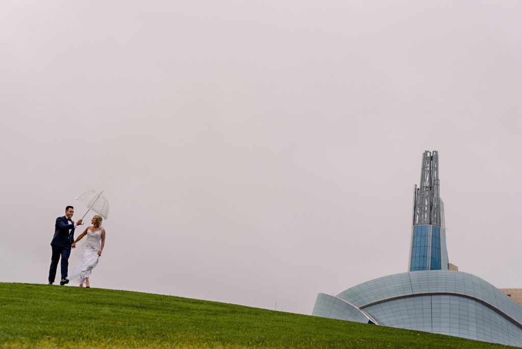 At Bride and Groom walking in the rain with an umbrella on a hill at the forks