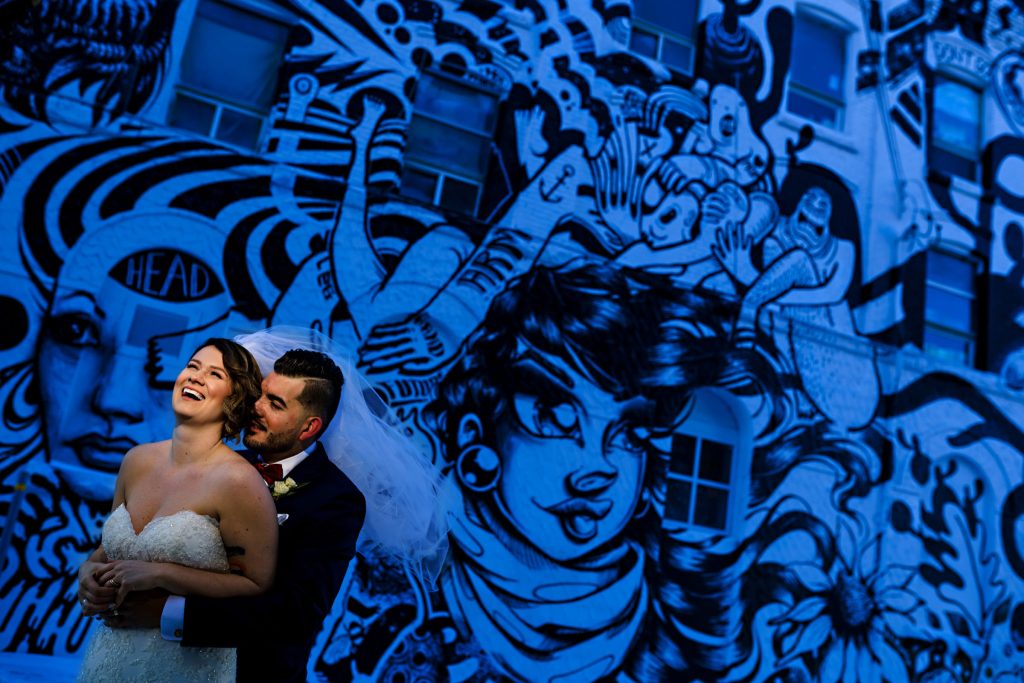 Bride and Groom embracing and laughing in front of a city mural in the winter