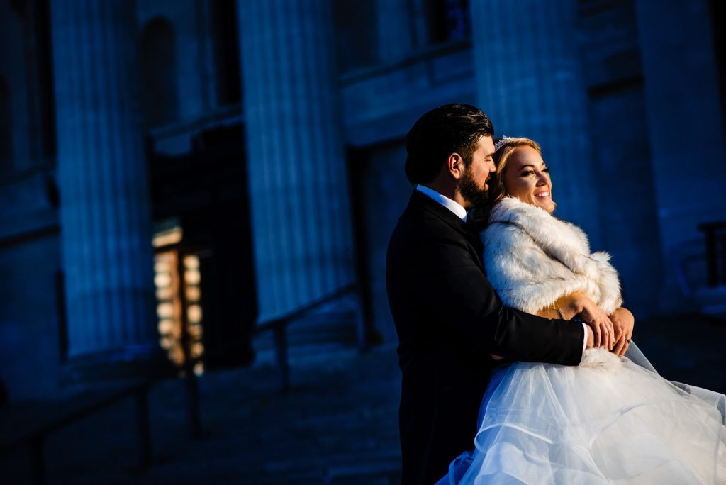Bride and groom, embracing for a wedding photo in front of the Winnipeg legislative building during winter