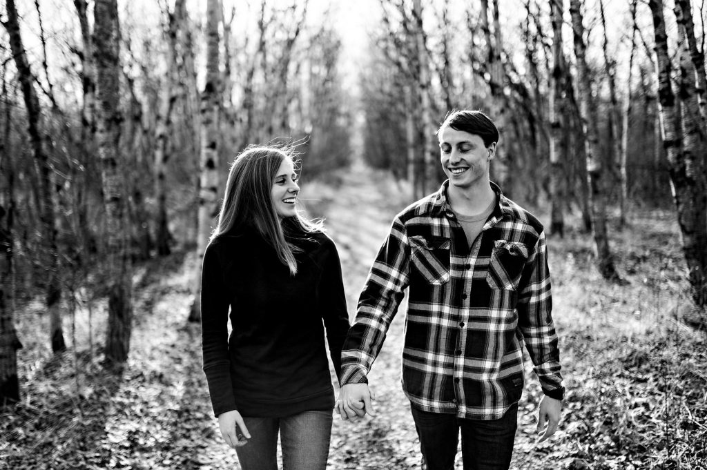 An engaged couple, holding hands and walking down a path at Assiniboine Forest
