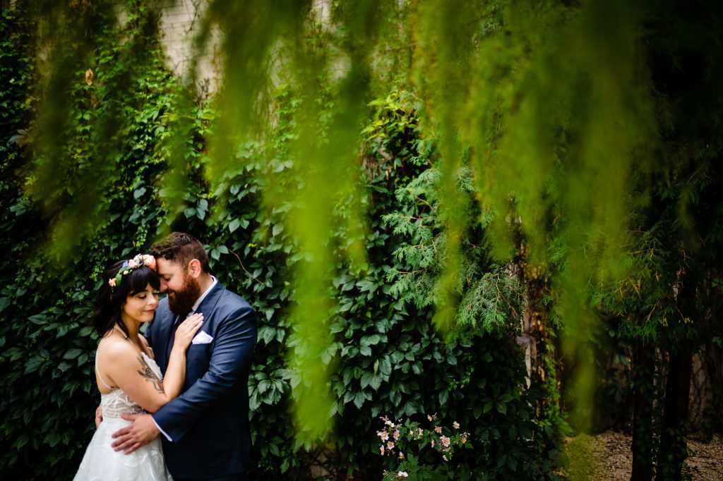 Bride and groom, embracing with their eyes closed in front of a green vine wall in Winnipeg Manitoba