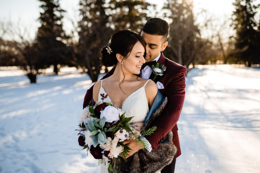 A bride and groom embracing each other on their wedding day in the snow, with Assiniboine forest in the background