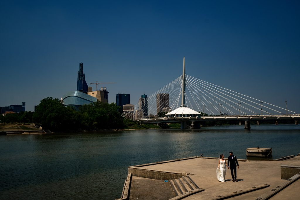 Room holding hands, and walking with the Winnipeg river and architecture in the background
