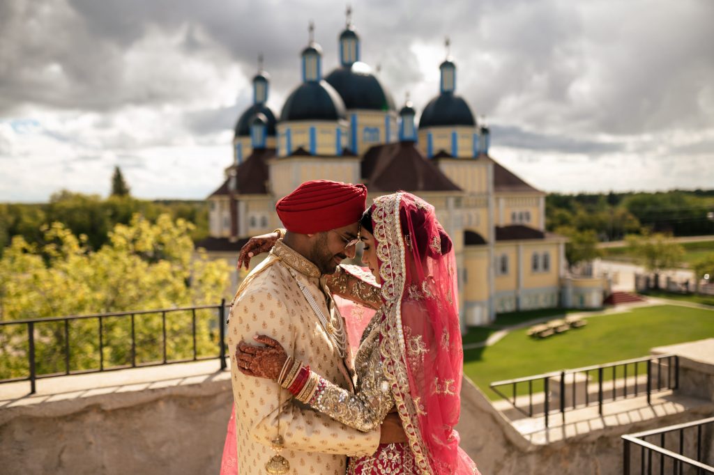 Bride and groom, embracing in front of a fancy building on a sunny day