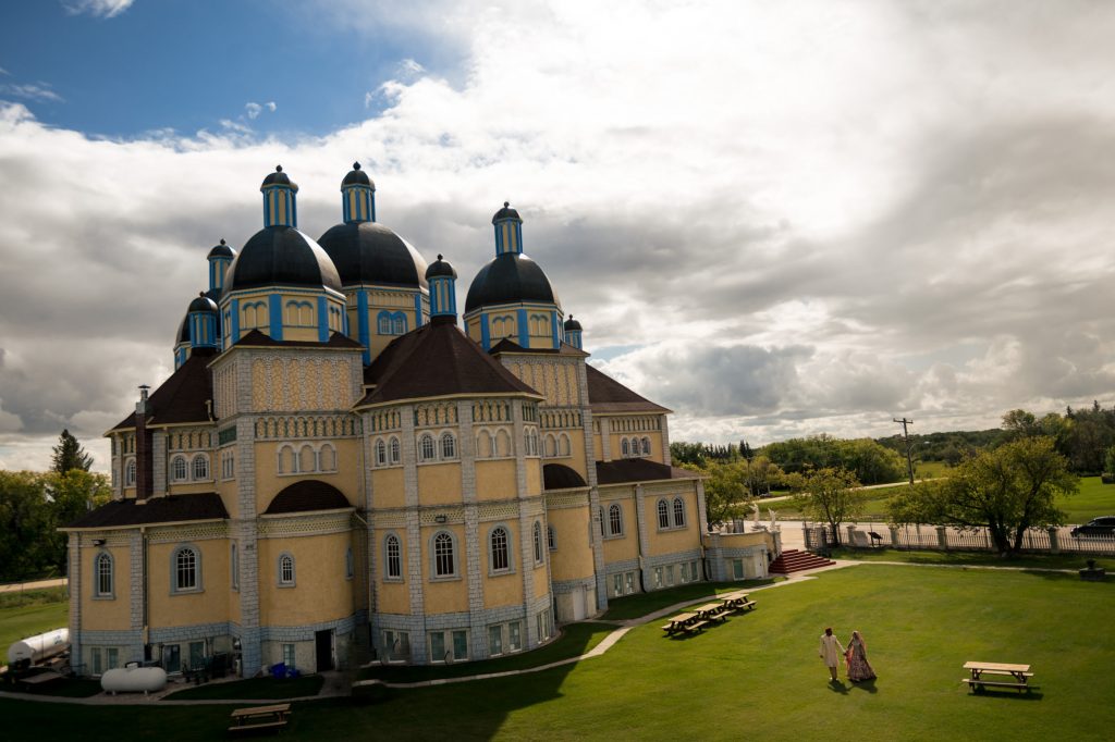 Bride and groom, holding hands and walking away from a Catholic church in Cooks Creek Manitoba