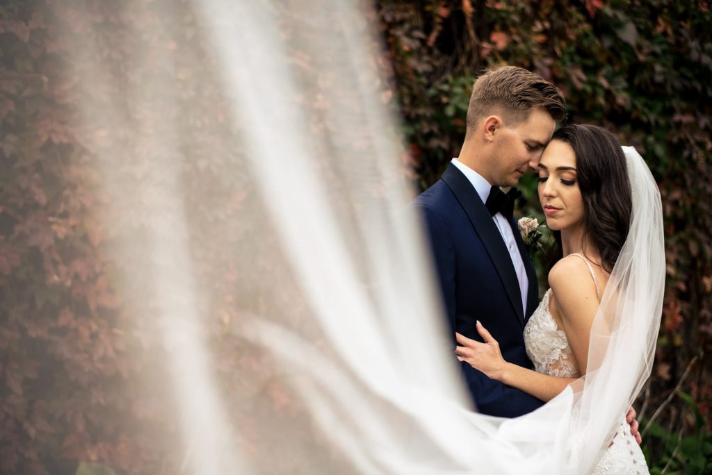 Bride and groom, embracing in front of a vine wall for a wedding photo