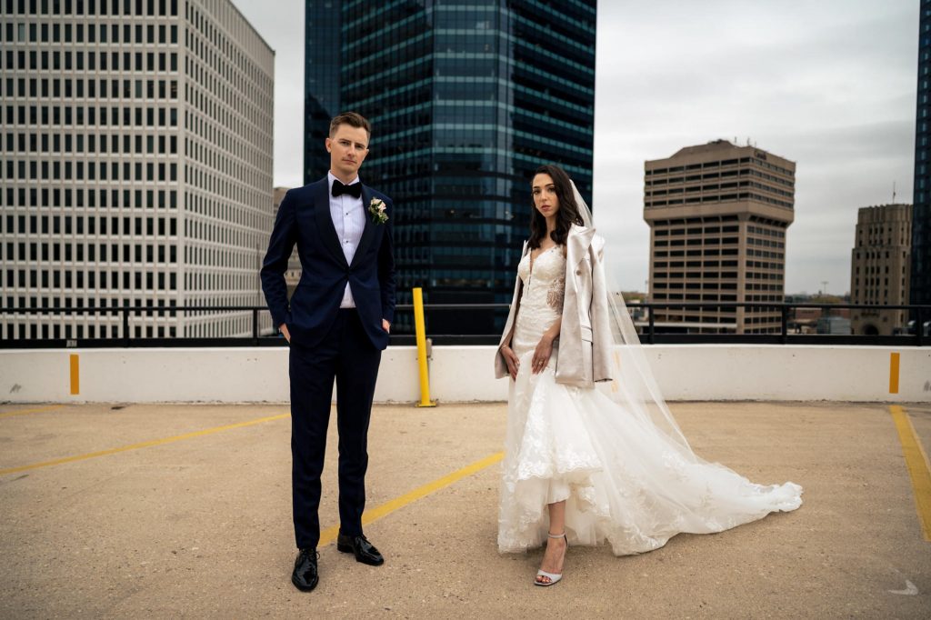 A bride and groom posing on a rooftop with buildings in the background in downtown Winnipeg