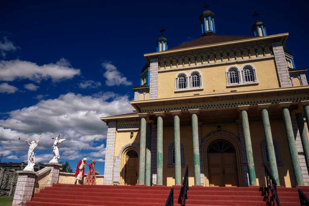 An Indian bride and groom posing for a photo next to a Catholic church at Cook's Creek Manitoba